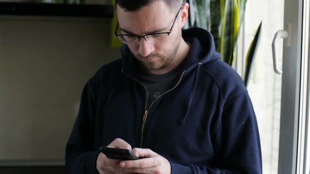 Young man using smartphone while standing by window at home