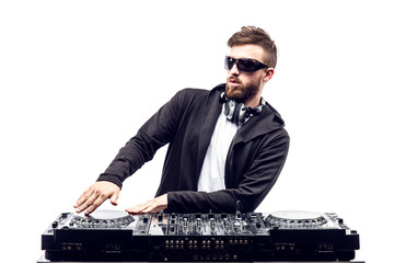 Young stylish man in black sunglasses posing with hands up behind mixing console on white studio...