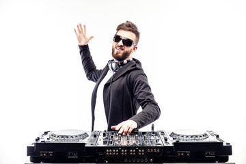 Young stylish man in black sunglasses posing with hands up behind mixing console on white studio...