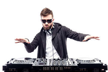 Young stylish man in black sunglasses posing with hands up behind mixing console on white studio background. - obrazy, fototapety, plakaty