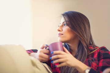 Attractive young woman drinking coffee at home looking to the window and daydreaming
