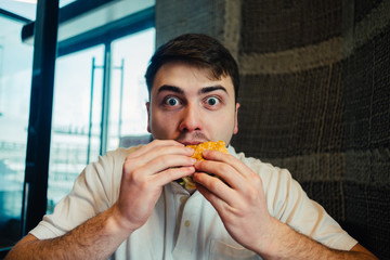 a young man eating a burger at the restaurant, and surprised his extraordinary taste