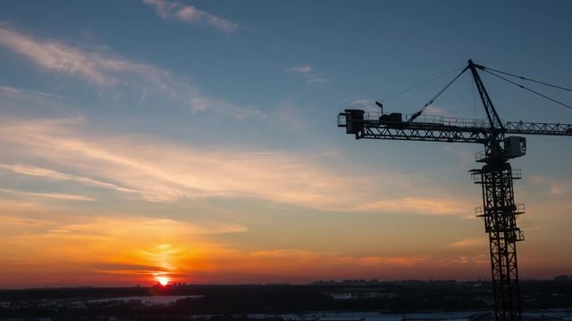 Timelapse with crane working on construction site on sunset sky background