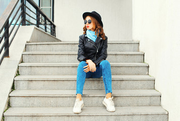 Fashion pretty young woman wearing a black rock jacket hat sitting in city
