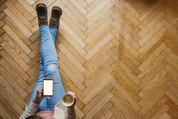 Girl with a smart phone having a coffee ona wooden floor