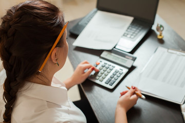 Young female bookkeeper considers on calculator - obrazy, fototapety, plakaty