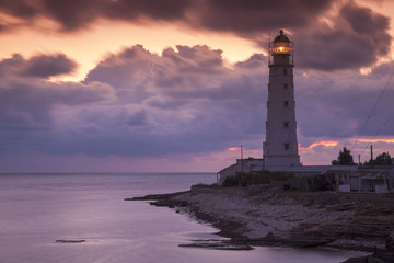 Fototapeta na wymiar colored sunset and lighting lighthouse on the sea coast