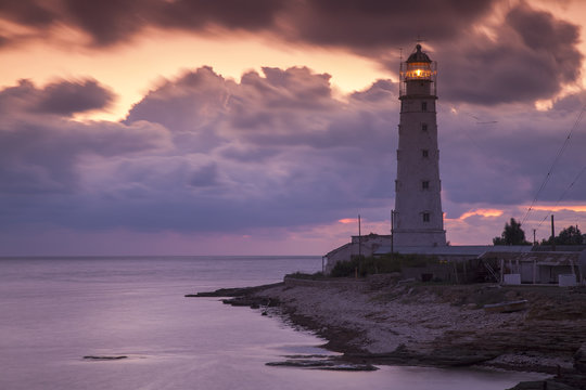 colored sunset and lighting lighthouse on the sea coast