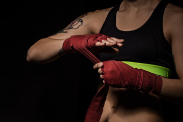 Woman wrapping hands with red boxing wraps in dark room. Close-up shot