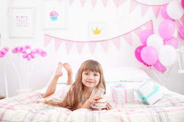 Obraz na płótnie Canvas Cute girl eating tasty cake while lying on bed in room decorated for birthday party