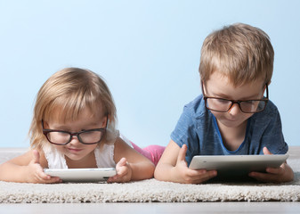 Cute funny children lying on carpet with tablet computer and mobile phone