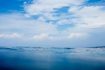 Obraz premium Glassy conditions on the ocean surface with ethereal clouds in the sky