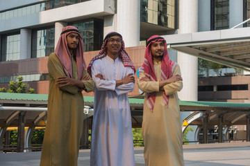 Three Arab businessman standing arms crossed, looking forward to the city.
