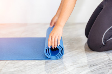 Close-up of attractive young woman folding blue yoga or fitness mat after working out at home in living room. Healthy life keep fit concepts.