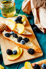 
sweet snack , bruschetta with berries and fruits , blueberries , blackberries and peaches , with butter and honey on wooden background