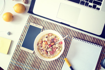 Healthy breakfast in front of computer laptop. oat porridge with smartphone notebook lemons note sticks on office table. Freelancers or programmer's workspace. Cozy workplace in tropical interior.
