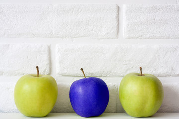 Group of healthy fresh apples with one different blue apple against white brick wall background. Team Idea. Generic modified food concept. Genius in business concept. Office creative work in team