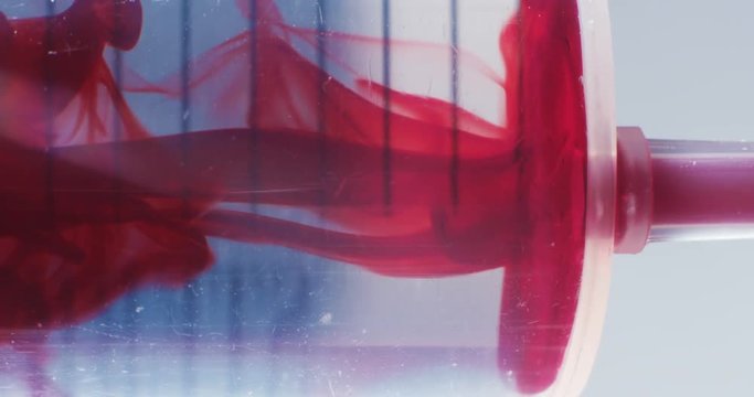 Macro shot of syringe pulling red liquid into saline solution against white backlight
