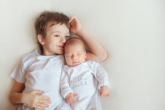 older brother hugging his newborn sister. Children in bright clothes on a white blanket.