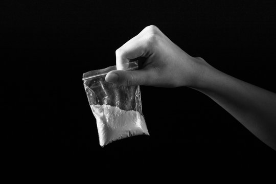 Packet With White Narcotic In Hand On Black Background, Monochrome