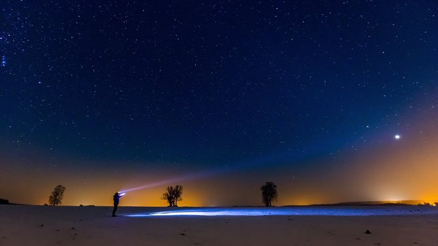 Starry sky and man with flashlight. Winter night landscape.