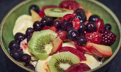 Healthy fruit salad in a green bowl with blueberries, kiwi, banana, plumb