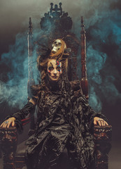 Young beautiful witch sits on a chair. Bright make up, skull, smoke-  halloween theme.