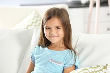 Portrait of cute little girl sitting on sofa at home