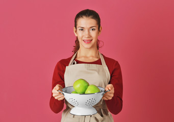 Woman holding apples in colander on color background