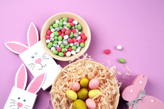 Easter concept. Paper bags with colourful eggs and candies on purple background - Powered by Adobe