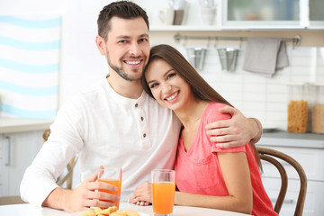 Obraz na płótnie Canvas Beautiful young couple with orange juice sitting at kitchen table