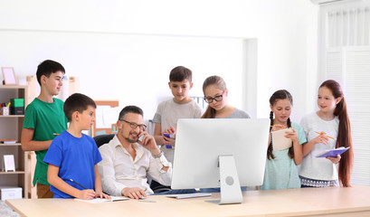 Male teacher working with computer while conducting lesson in classroom