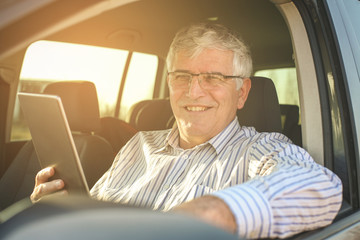 Senior man using digital tablet in a car.