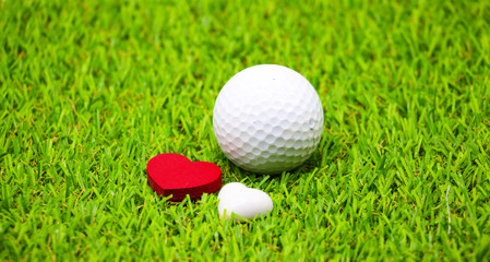 Golf ball with red heart shape on green grass