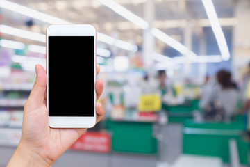 Woman hand holding mobile phone at supermarket checkout background