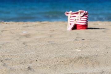 Beach tote on a sandy beach with a blue sea on the background. Selective front focus on the sand