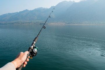 man holding fishing rod, fishing pole over the lake.