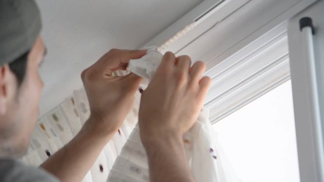 Young handsome man or handyman installing curtains over window at home, doing renovation work