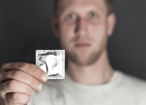 
Hand of  young man holds packing of condoms. Blurred face
