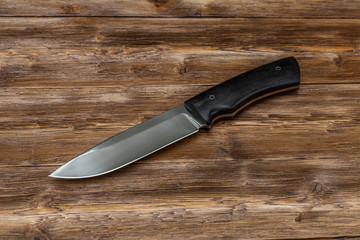 Hunting steel knife handmade on a wooden background, close-up
