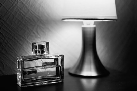 Table lamp with shade burlap burning on a wooden table and a bottle of men's fragrances. Black-and-white picture.