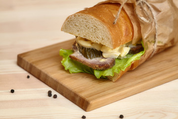 Big sub sandwich baguette with ham on wooden cutting board