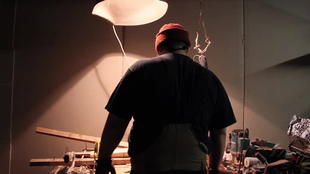 Fat craftsman prepares to work turning light on in his workshop