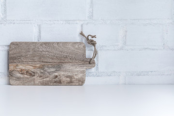 Cooking concept - simple laconic kitchen background: white table, wooden kitchen board against white brick wall background. Copy space.