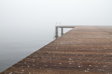 A wooden pier and stairs to sea in a foggy day. Most of the photo is covered with the wooden pear.