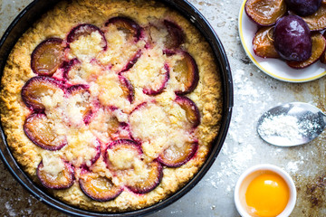 Plum Cake Dessert with Raw Cooking Ingredients on Wooden Kitchen Table