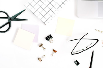 White office desk frame with paper blank and supplies. Laptop, notebook, scissors, pen, clips, glasses and office supplies on white background. Flat lay, top view, mockup.