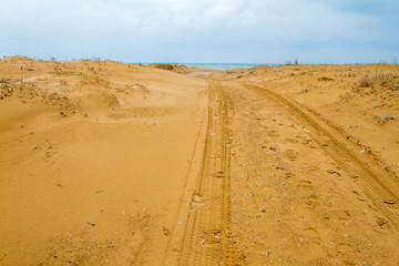Photo of a sandy road to beach.  There is only sand until the sea. Tyre trails are also visible.