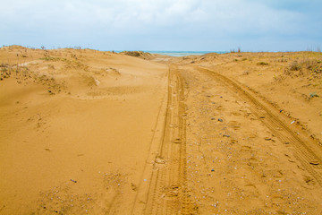 Photo of a sandy road to beach.  There is only sand until the sea. Tyre trails are also visible.