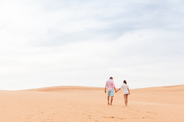Fototapeta na wymiar Young Man Woman Walking In Desert Couple Girl And Man Hold Hands Back Rear View Sand Dune Landscape Background